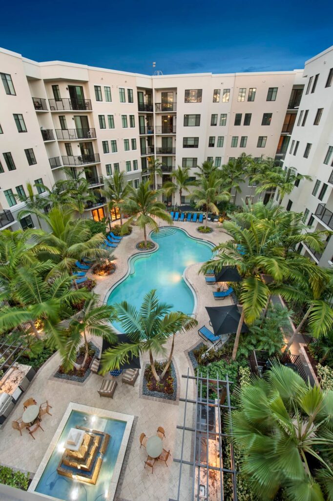 Aerial view of pool courtyard with deck seating and palm trees, as well as outdoor grilling stations